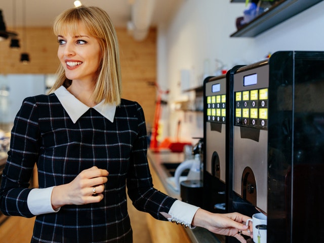 Verpflegungsautomaten in Betriebsstätten und Büros Junge Frau die sich einen Kaffee am Automaten zieht