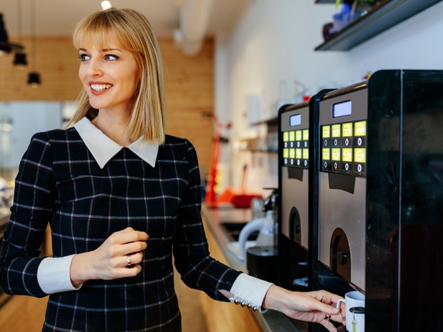 Junge Frau die sich einen Kaffee am Automaten zieht